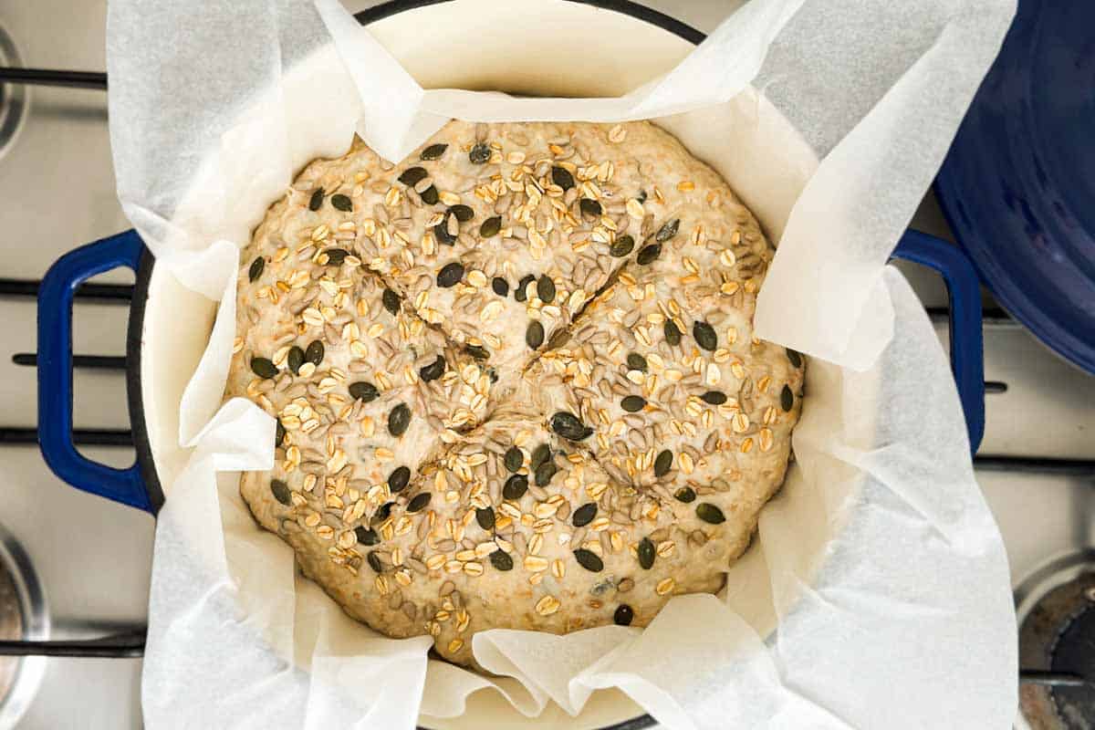Dough in the parchment-lined Dutch oven before baking, topped with oats and seeds.