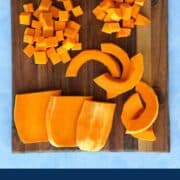 Fresh butternut squash being cut into cubes on a wooden cutting board.