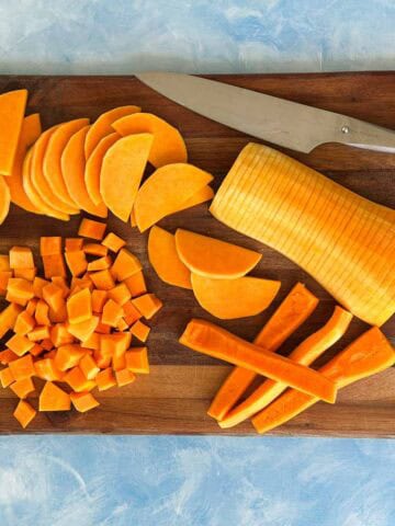 Butternut squash prepared in different cuts on a wooden board, including cubes, half-moon slices, wedges, and thin slices, with a chef's knife.