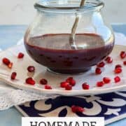 Glass jar of homemade pomegranate molasses with pomegranate seeds.