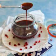 Thick homemade pomegranate molasses dripping from a spoon back into a glass jar, with pomegranate seeds scattered on the plate.