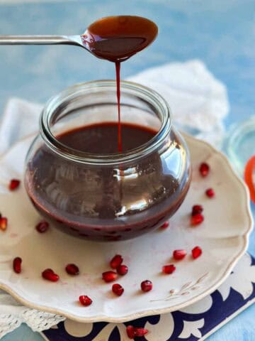 Thick homemade pomegranate molasses dripping from a spoon back into a glass jar, with pomegranate seeds scattered on the plate.