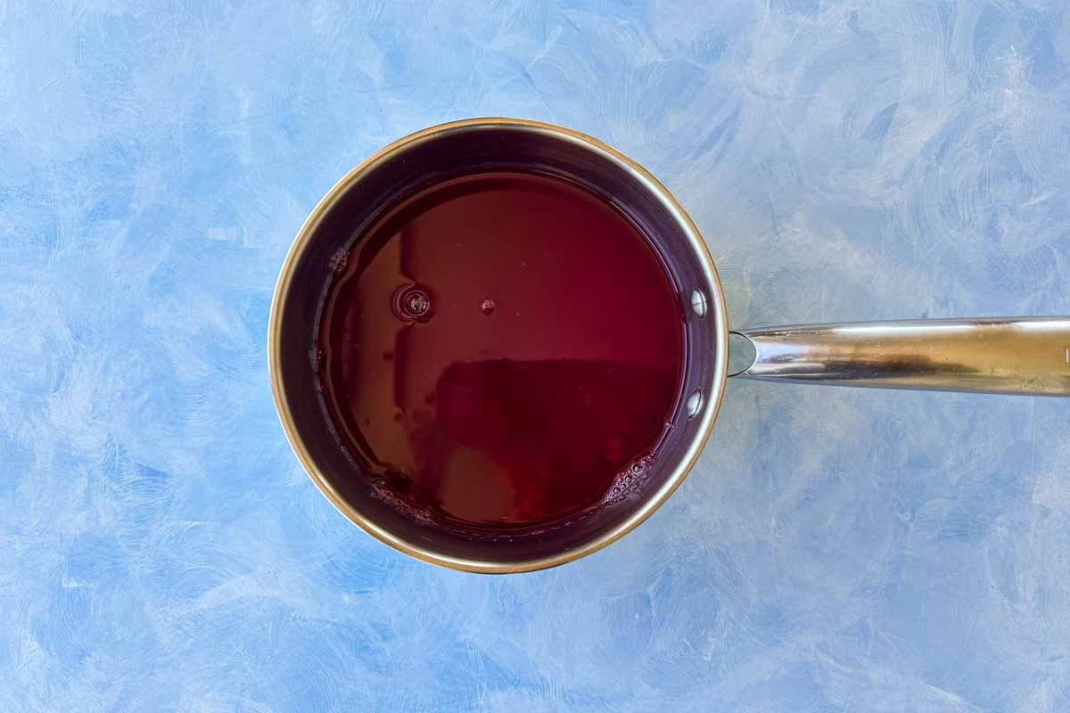 Pomegranate juice in a saucepan on a blue background, ready to simmer for homemade pomegranate molasses.