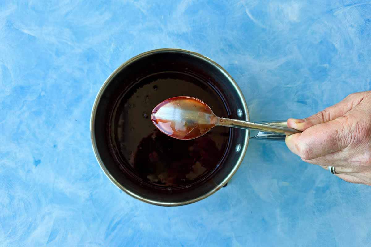 Thickened pomegranate molasses in a saucepan with a spoon showing the glossy syrup texture.