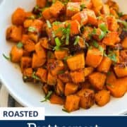 Delicious roasted butternut squash cubes garnished with herbs on a white plate.