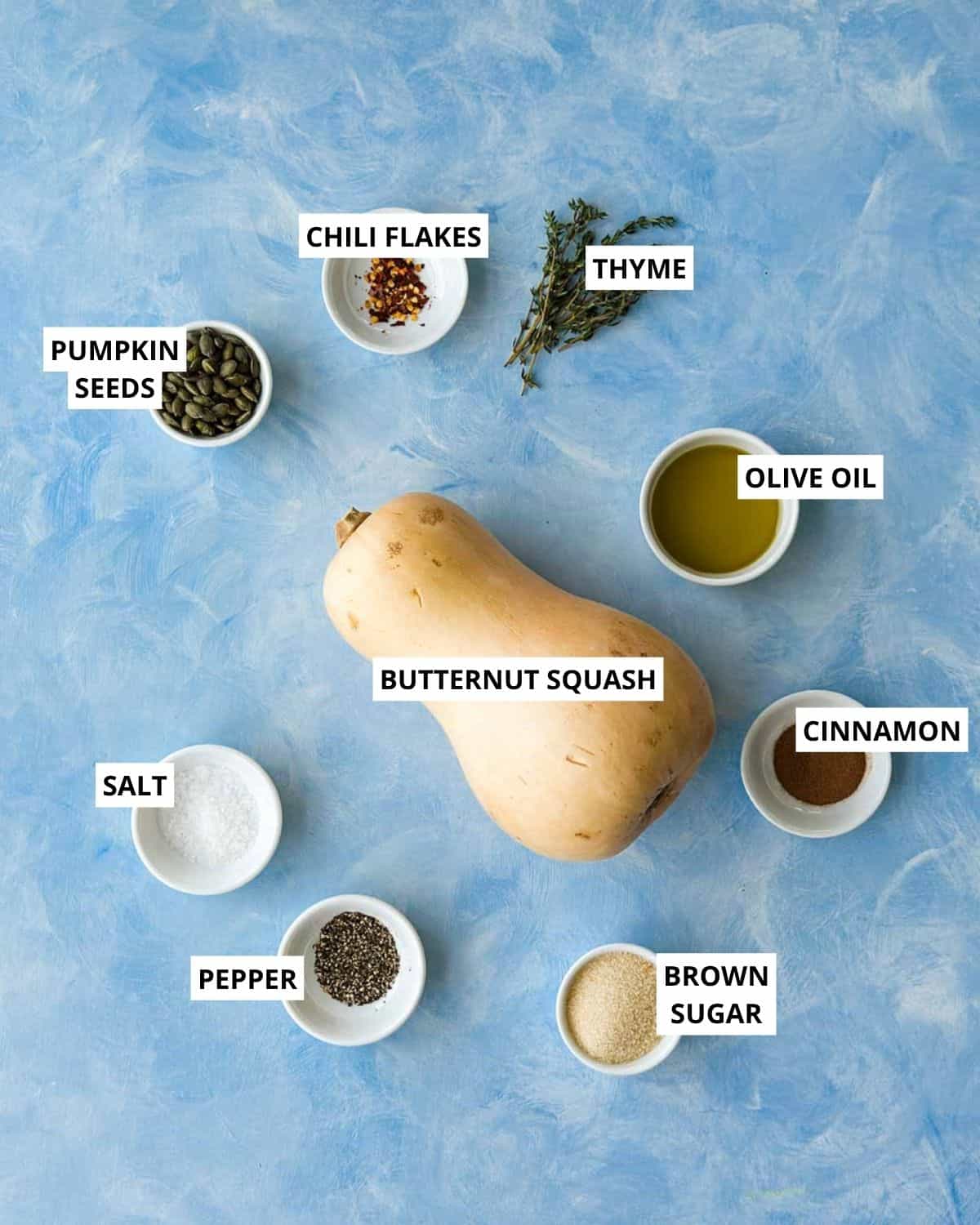 Ingredients for cinnamon roasted butternut squash slices, including butternut squash, pumpkin seeds, thyme, chili flakes, olive oil, cinnamon, brown sugar, salt, and pepper.