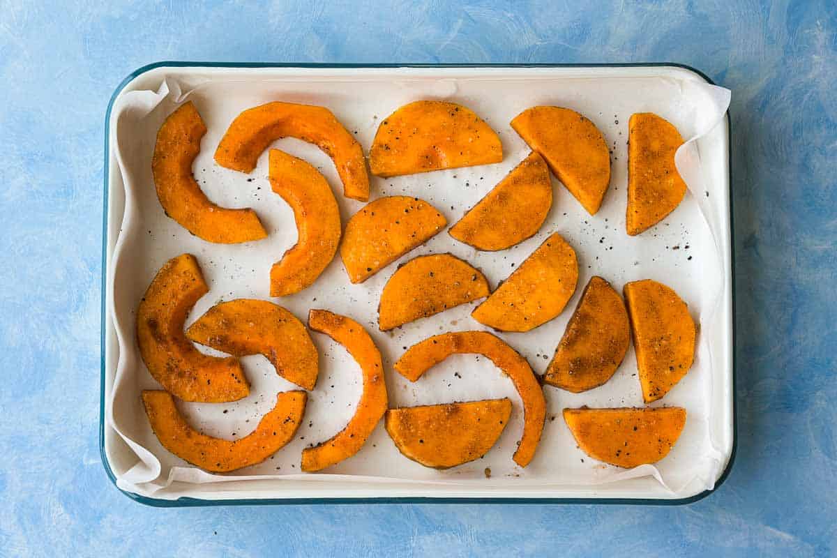Seasoned raw butternut squash slices arranged in a parchment-lined baking dish before roasting.