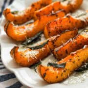Roasted butternut squash wedges with browned edges, herbs, sage leaves, and grated Parmesan cheese for a simple fall vegetable side dish.