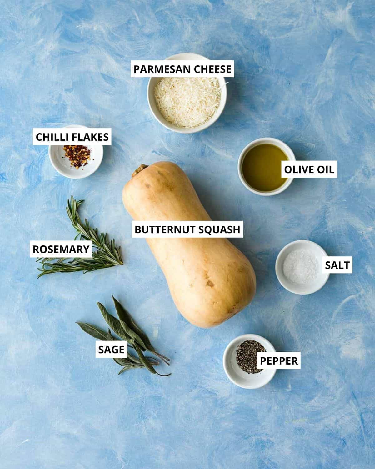 Ingredients for roasted butternut squash wedges, including butternut squash, Parmesan cheese, olive oil, rosemary, sage, chilli flakes, salt, and pepper.