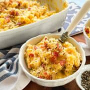 Close-up of a scalloped white bowl of butternut mac and cheese with bacon and breadcrumbs, a spoon resting in the pasta.