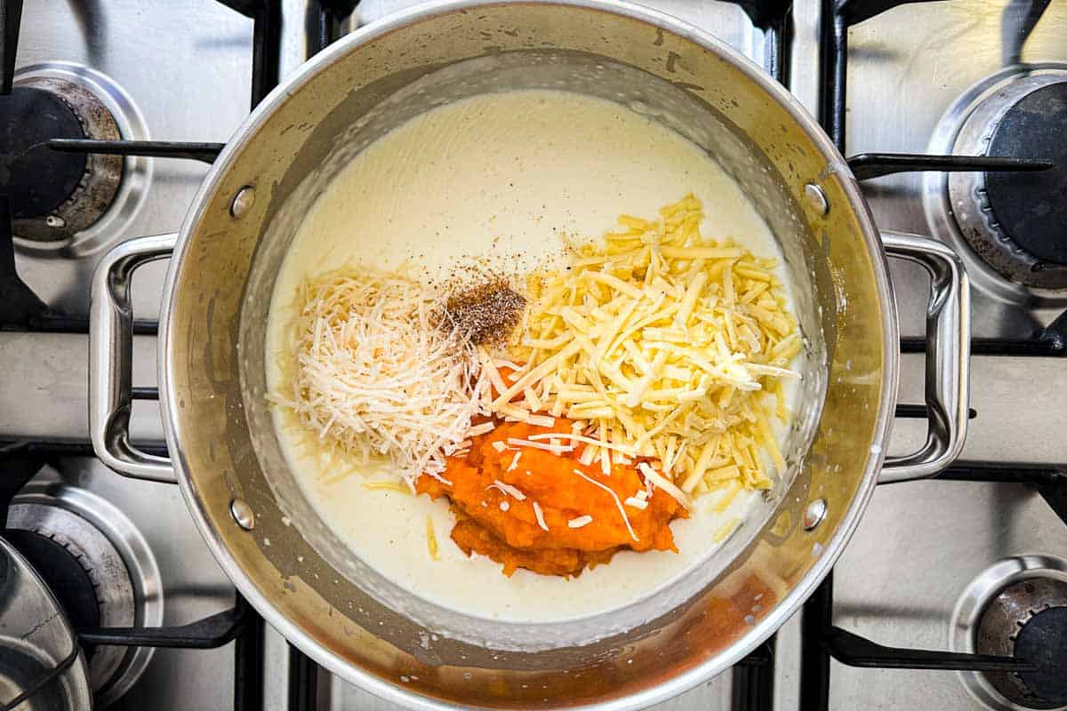 Parmesan, cheddar, butternut squash puree, and nutmeg added to a creamy white sauce in a pot, before stirring.
