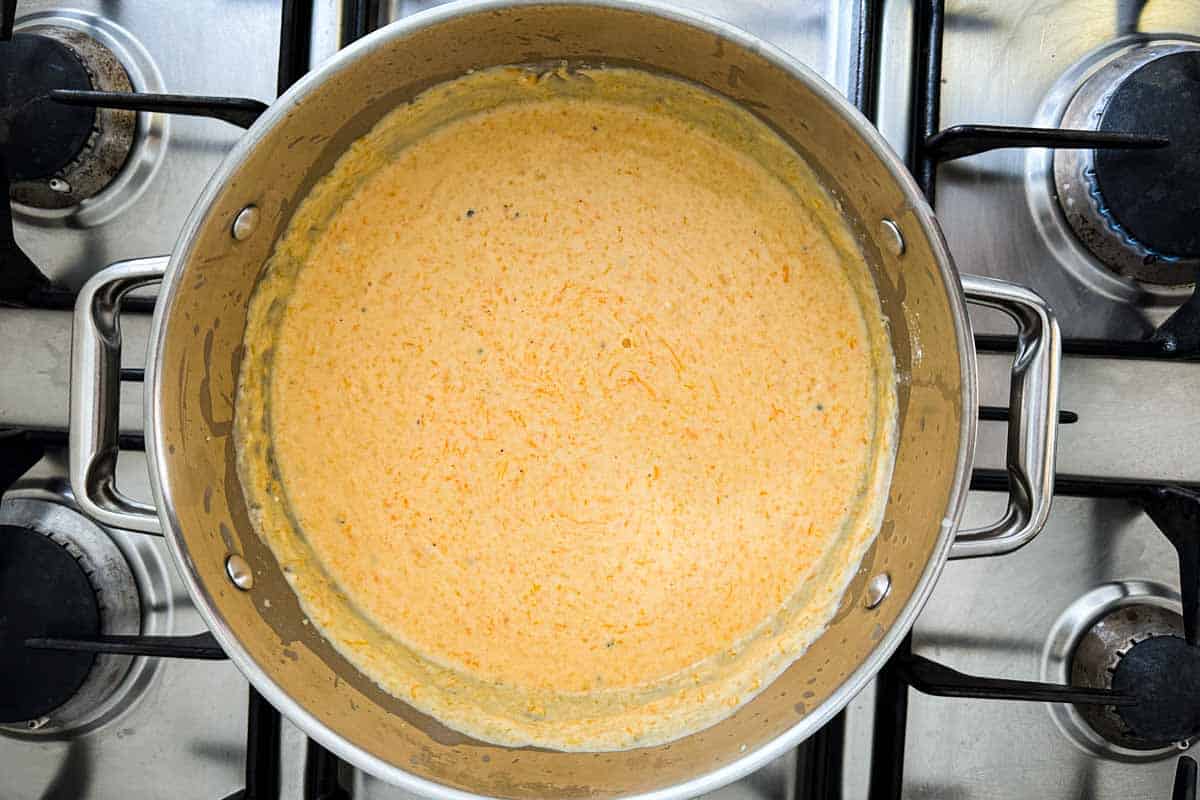 Smooth, orange butternut cheese sauce in a large stainless steel pot on the stove.