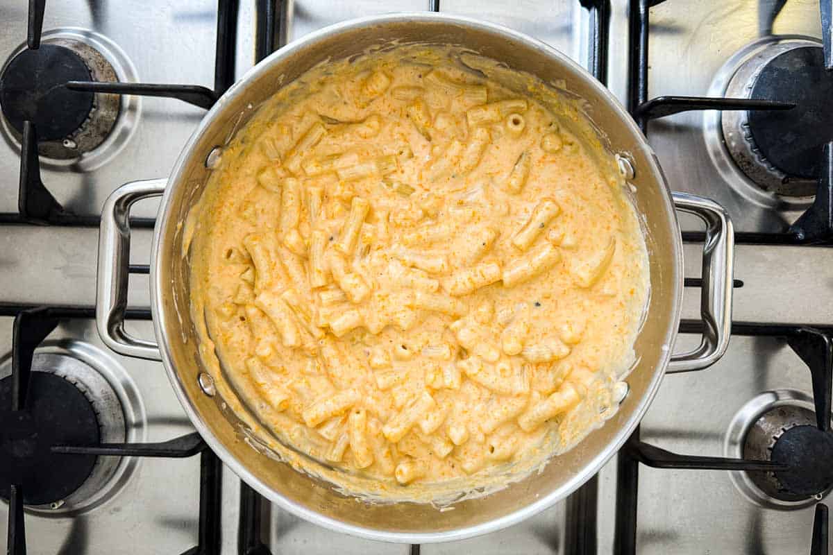 Short pasta stirred into the creamy orange butternut cheese sauce in the pot.