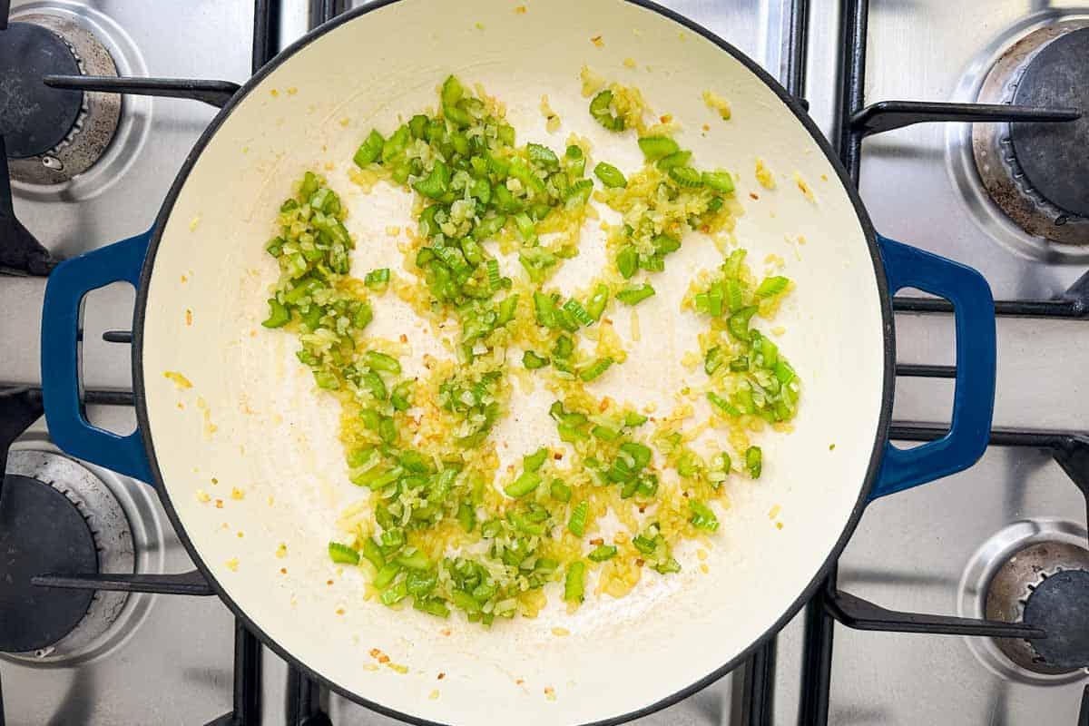Chopped celery and onion sautéing in a Dutch oven on the stovetop.