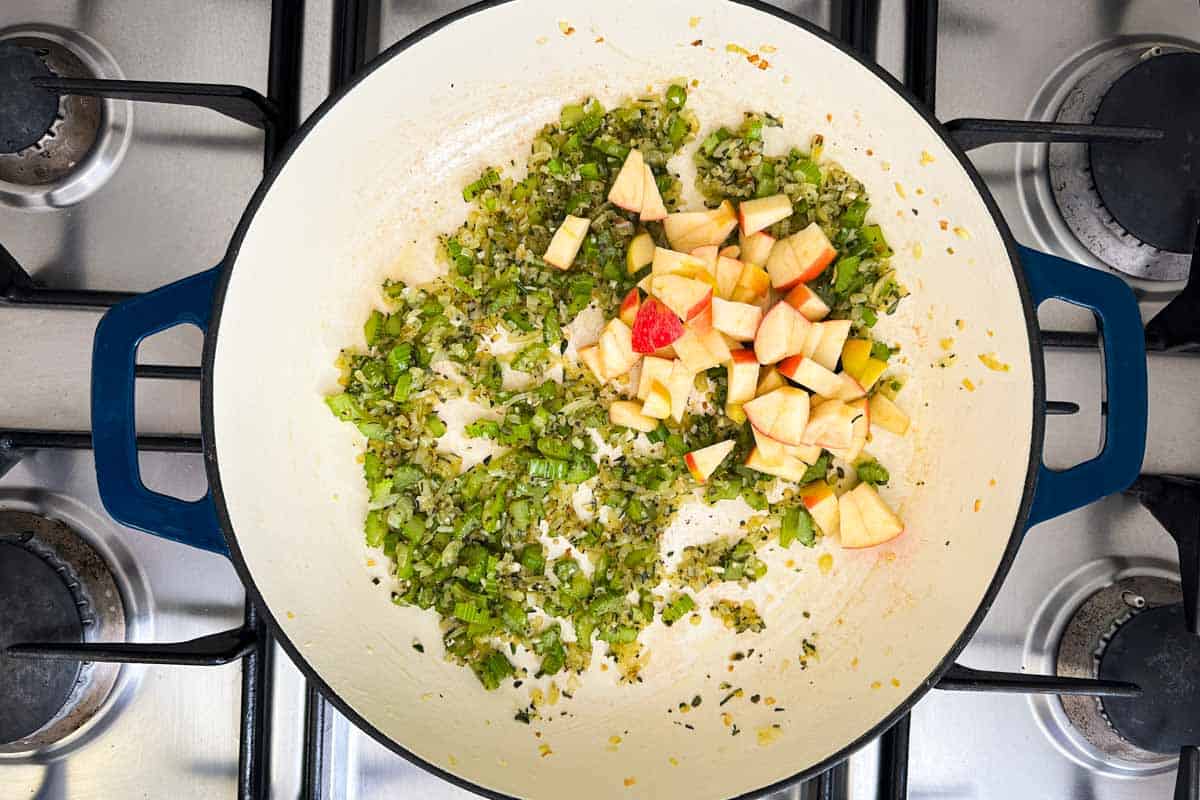 Diced apple added to the sautéed onion, celery, and herb mixture in the pot.
