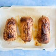 Overhead view of three whole roasted butternut squash, skins blistered and browned, on a parchment-lined baking dish.