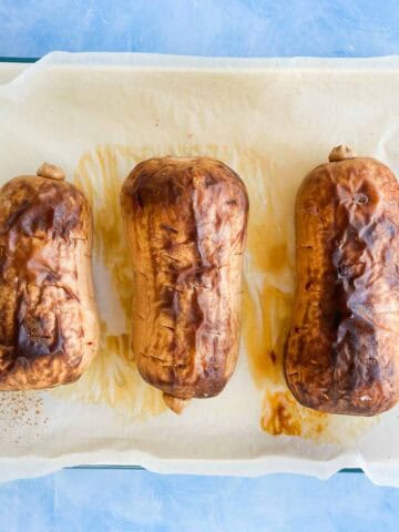 Overhead view of three whole roasted butternut squash, skins blistered and browned, on a parchment-lined baking dish.